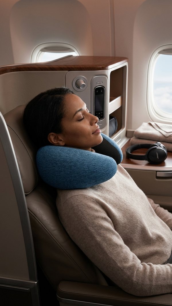 A woman resting her head on a contoured travel neck pillow in a business class seat