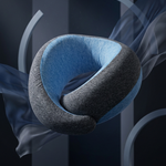 A modern U-shaped neck pillow with a textured dark gray outer shell and a soft blue inner cushion, floating in a dark, abstract studio setting with flowing translucent blue fabric.