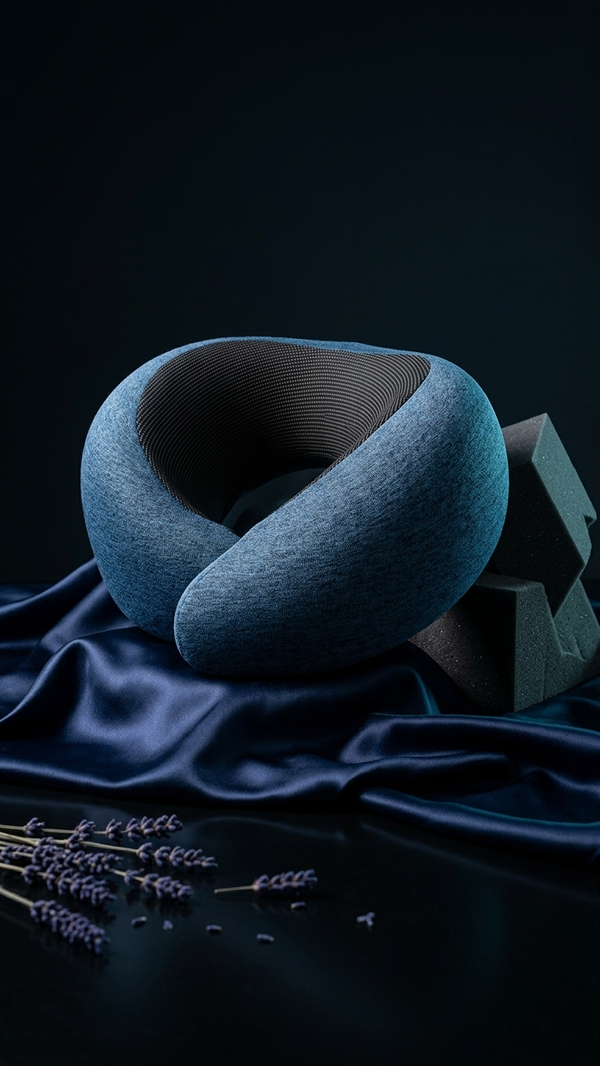 The Cloud Rest Pod contoured neck pillow in blue-grey, styled on navy satin
