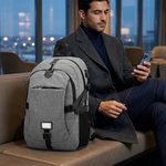A man in a dark coat sits on a tan leather bench in a modern lounge, looking at his phone next to a gray and black backpack.