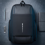 A dark gray backpack with a vertical white logo, displayed on a dark gray textured background with a pen, a smartphone, and a notebook as props.