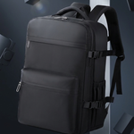 A black multi-compartment backpack with padded shoulder straps and side compression buckles, shown floating in a dark gray studio setting with geometric props.