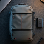 A gray and black laptop backpack is shown from a top-down perspective on a dark textured desk, styled with a silver laptop, a small black electronic device, and a notebook.