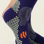 A close-up of a person's foot and ankle wearing a pair of navy blue grip socks with green dotted traction patterns and an orange logo on the sole.