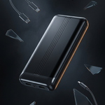 A sleek black portable power bank with a metallic finish, shown floating at an angle with various transparent glass shards and USB-C cables scattered around it on a dark background.