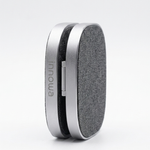 A slim, oval-shaped portable speaker by Innowa, featuring a textured gray fabric grille and a metallic silver aluminum frame, standing upright on a light gray background.