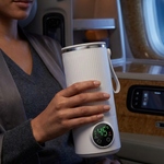 A woman in a gray lounge setting holds a white ribbed insulated travel tumbler with a digital temperature display on the front.