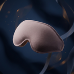 A soft, blush pink sleep mask floating against a dark navy blue background with flowing ribbon-like textures and subtle warm light specks.