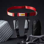 A red and black safety harness with gray padded shoulder straps, displayed on a dark surface with a silver hard case, a black pouch, a rolled black strap, and a gray cloth.