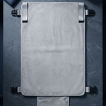 A light gray padded rectangular pouch or cover with black strap hardware, laid flat on a dark textured surface. A matching small pouch hangs below it, and a dark blue notebook and gray headphones are placed at the top corners as props.