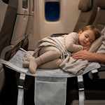 A child sleeps on a gray airplane seat tray table with a blanket, set inside an airplane cabin.