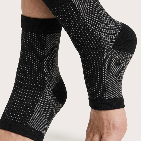 Black ankle support sleeves with a textured mesh pattern, shown on a person's feet against a light gray background.